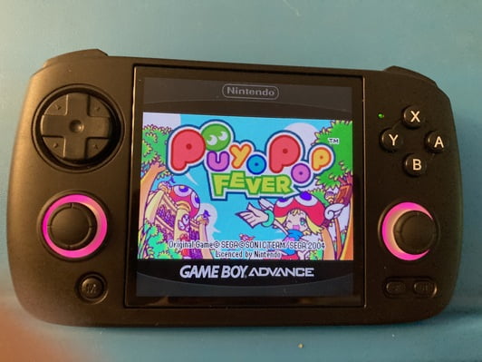 close up of a small black handheld gaming console with pink LED lights around the joysicks